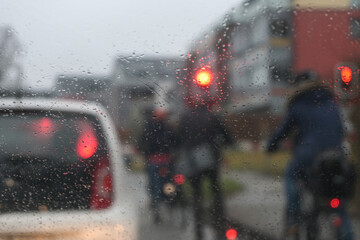 Raindrops on the windshield while waiting in front of a red traffic light, blurry cyclists, car and...