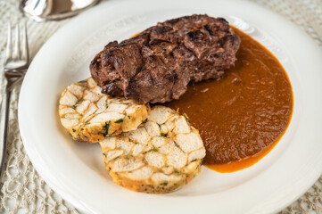 Deer meat with plum sauce and dumpling on plate, on white table, closeup