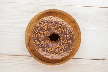 One sweet chocolate doughnut on a wooden saucer, on a wooden table, macro, top view.