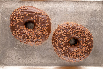 Two sweet chocolate donuts on a metal tray , macro, top view.