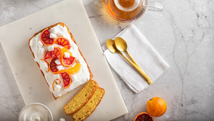 orange sponge cake garnished with fresh bloody oranges and cream and glass teapot on marble...