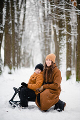 Fototapeta na wymiar Mother and son sitting on sledge at snowy forest