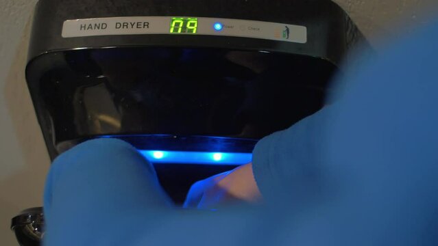 Close-up view of woman drying hands after washing in modern air hand dryer