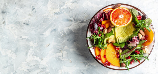 Healthy vegetarian buddha bowl salad with avocado, persimmon, blood orange, nuts, spinach, arugula and pomegranate on a light background, Long banner format, top view