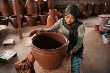 girl in headscarf shapes clay into pots on wheels