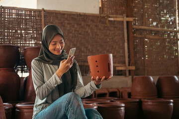 girl in hijab using mobile phone camera to photograph pottery