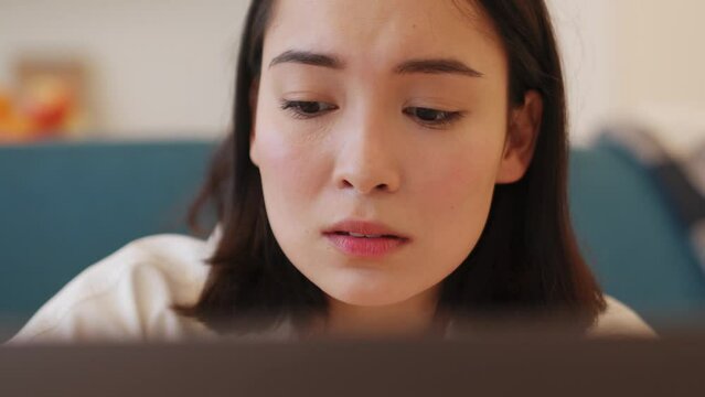 Sad Asian woman working on laptop at home