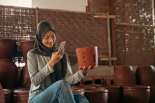 girl in hijab using mobile phone camera to photograph pottery
