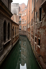 Fototapeta na wymiar Die Roten Fassaden Venezianischer Häuser spiegeln sich im ruhigen Wasser eines Wasserkanal