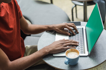 Cropped view of african american freelancer using laptop with chroma key near coffee in cafe.