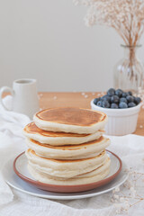 Vertical image of a simple traditional stack of pancakes without any sauce or butter. Fruit, flowers and jug on top a wooden table. Copy space available in light airy backdrop