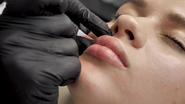 A cosmetologist applies permanent makeup to the lips in a beauty salon. Tattoo