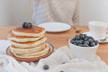 Breakfast pancakes scene with person pouring syrup or sauce over the stack. Rustic light and airy feel with white light background and copy space available.