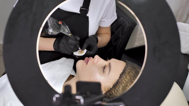 A cosmetologist applies permanent makeup to the lips in a beauty salon. Tattoo
