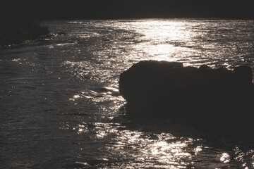 rapid water with reflection of sunlight, silhouette of large granite boulder