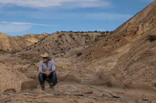Adult man in cowboy hat sitting on rock in Tabernas desert. Almeria, Spain