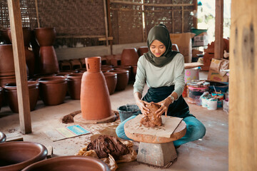 veiled girl making clay pottery on wheels in studio workshop