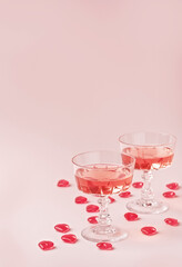 Two crystal glasses of rose sparkling wine or champagne and red glass hearts on pastel pink background. Happy Valentines Day concept. Minimal creative composition with copy space.