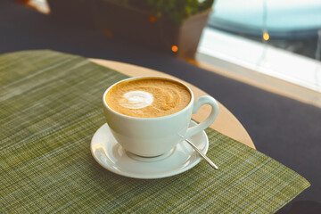 A large white cup of freshly brewed cappuccino with vegetable milk. Hot coffee with colorful latte art on the table. Coffee break in the afternoon