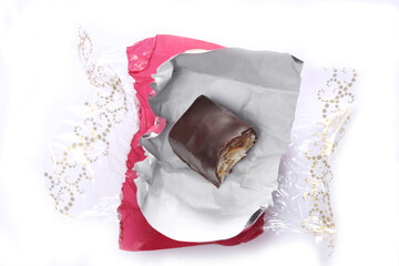 bitten chocolate candy  in a red open wrapper isolated on white background with copy space for your text.