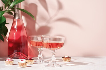Two crystal glasses of rose sparkling wine or champagne and chocolates on pastel pink marble table in sunlight. Minimal creative composition with copy space. Summer drink concept.