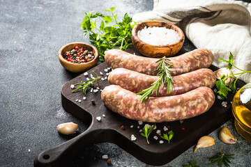 Bratwurst or sausages on cutting board with spices and herbs at dark table.