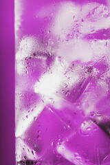 Ice cubes in a glass with refreshing ice water on a pink background.