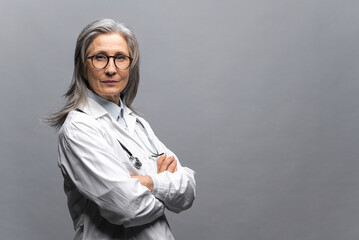 Headshot of intelligent professional mature female doctor with gray hair, wearing glasses, medical...