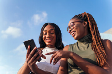 two young african women having fun looking phone - Powered by Adobe