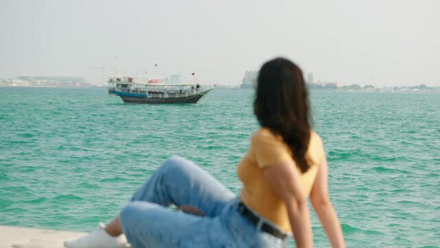 Tourist woman at corniche watching dhow boat passing on west bay at Doha Qatar
