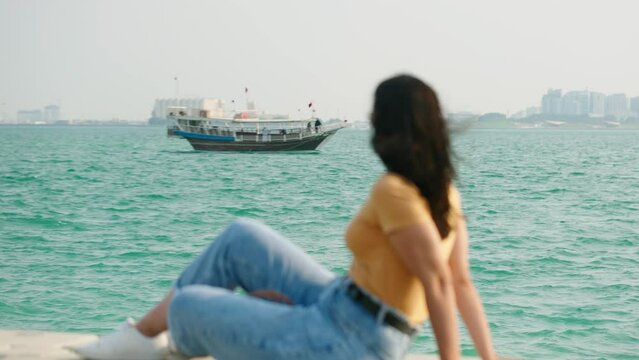 Tourist woman at corniche watching dhow boat passing on west bay at Doha Qatar

