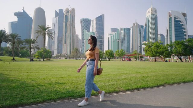 Woman tourist walking with skyline of Doha seen from Al Dafna Park. Mordern skyscrapers and towers on background
