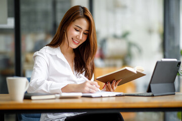 Portrait of smiling happy beautiful Asian woman relaxing using technology of laptop computer while sitting on table.Young creative girl working and typing on keyboard at cafe.work at home concept