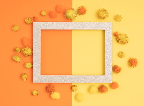 Empty gold picture frame with pom-poms on orange and yellow background. Romantic Valentines day composition. Flat lay. Love concept.
