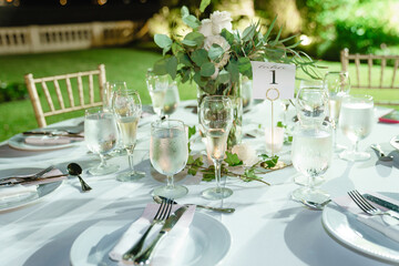 Wedding table decorated with bouquets of white roses Served table for dinner on the wedding party at the luxury hotel restaurant Table set up for a special event with roses and greenery outdoor