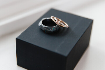Two wedding rings on the black box Close up of the diamond gold ring of the bride and black ring of the groom Wedding details of the newlywed's couple
