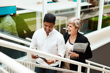 Levelling up together in business. Shot of two businesspeople walking up a staircase together in an office.