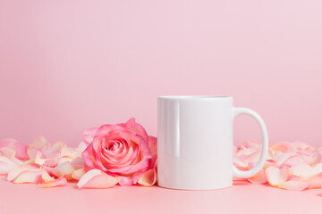 Fototapeta na wymiar White mockup mug or coffee cup on pink background with rose and petals. Blank mug for template, branding, text or design