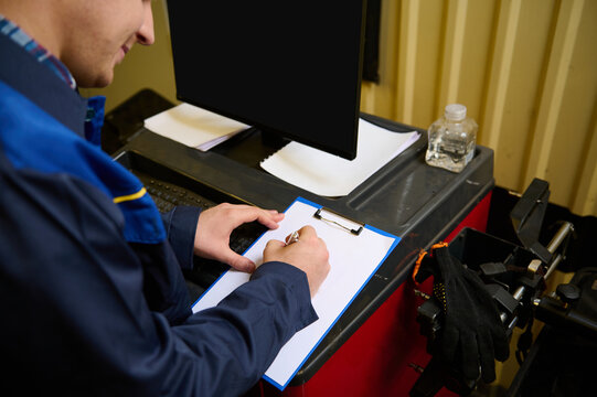 Rear view of a technician, garage mechanic writing on clipboard with blank white paper sheet, doing check lists for repairing car during regular warranty service in the repair shop