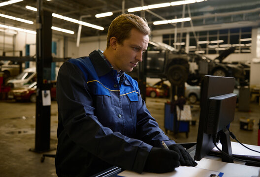 Concentrated auto mechanic technician car engineer writing checklist on clipboard and working on monitor while servicing a car in the auto service