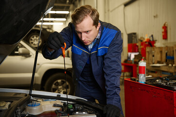Fototapeta premium Car engineer technician mechanic in professional uniform checking oil level in car engine while doing repair and maintenance in the automobile in the repair shop garage.