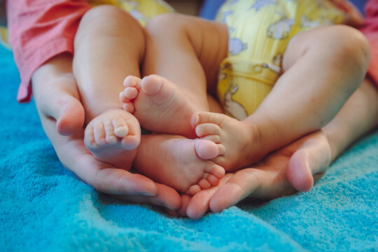 Mother Holding In Hands Feet Of Newborn Twin Babies