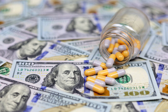 Pills in capsules scattered from a bottle on US dollars currency. Concept of health care in USA, pharmaceutical business, drug prices, pharmacy, medicine and economics