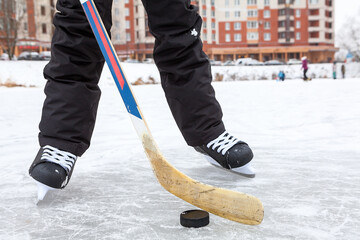 Forward holding black puck with stick, hockey skates on lake ice, teenage male legs, front view
