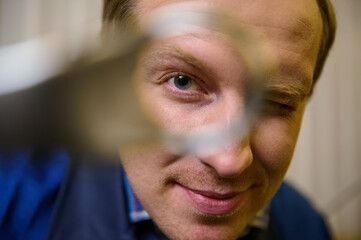 Close-up portrait. Headshot of Caucasian man, technician, auto mechanic looking at camera through a wrench in his hand. Labor, people, professional occupation, consumerism and service concept
