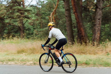 Athletic man rides a bicycle in nature, wears sports equipment.