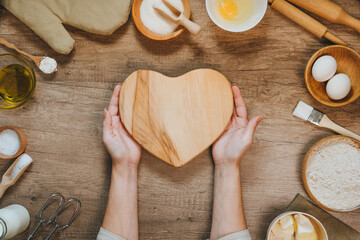 Heart shape wooden board near ingridients for prepairing dough
