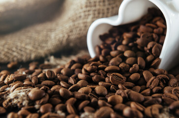 Coffee beans . Coffee beans pouring out of heart shaped cup on fabric and wooden background