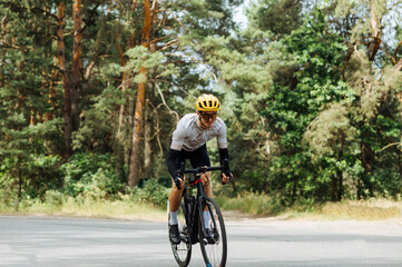Naklejka premium Male cyclist in a helmet and sports equipment rides a bicycle on a forest road with a smile on his face.