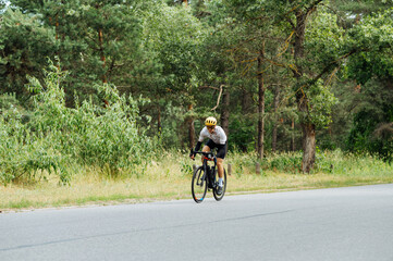 Professional cyclist sportsman trains in the woods on an asphalt road. Active rest.
